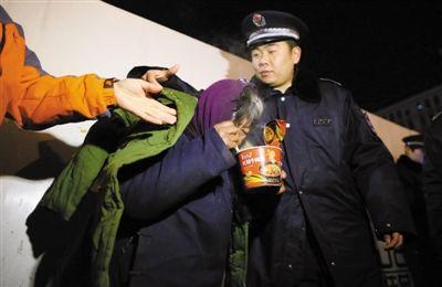 昨晚，西单，西城城管联合公安等部门救助街头流浪乞讨人员，一名城管队员给乞讨的大妈披上大衣，送上热的方便面。新京报记者 薛珺 摄