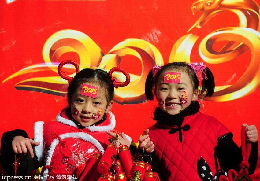 2012年12月31日，江西省九江小学的学生额头贴着蛇形节庆图案，手拿新年饰品在印有“2013”字样的展板前拍摄合影。佚名/东方IC 